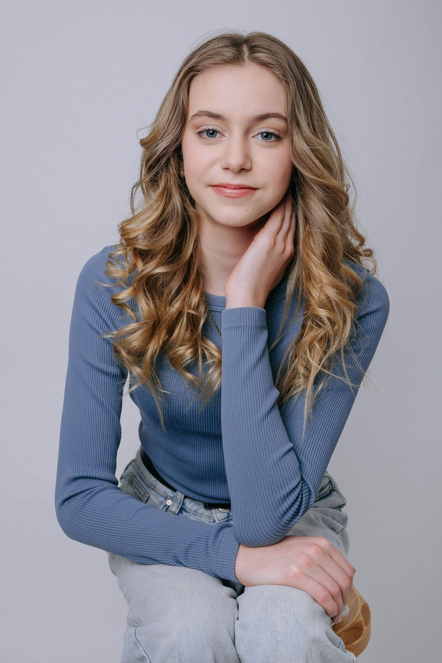 A series of studio portraits showing a person in a blue sweater and light jeans against a gray background.