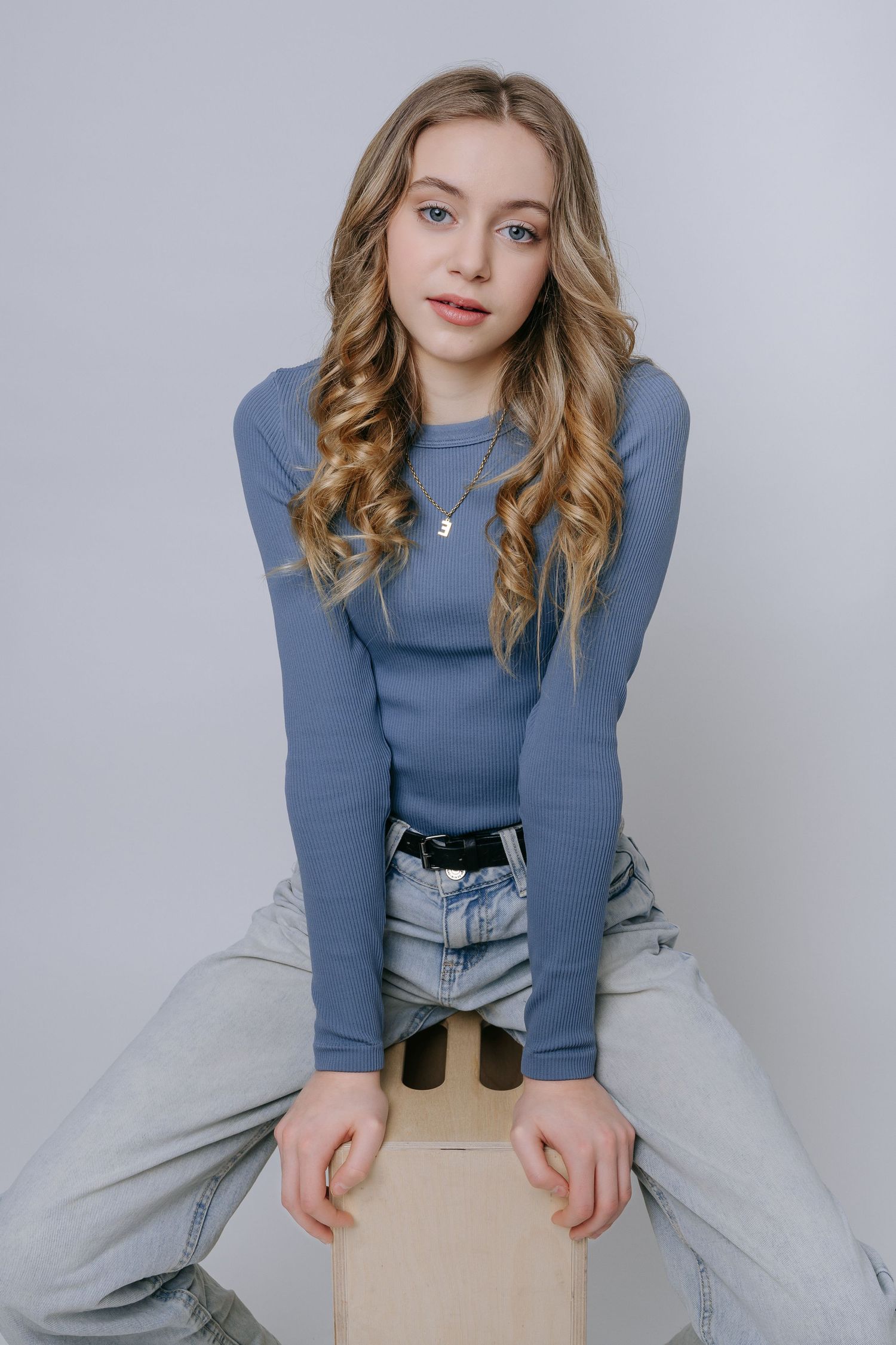 Fashion model poses in blue ribbed sweater and light jeans against white backdrop in casual studio photoshoot.