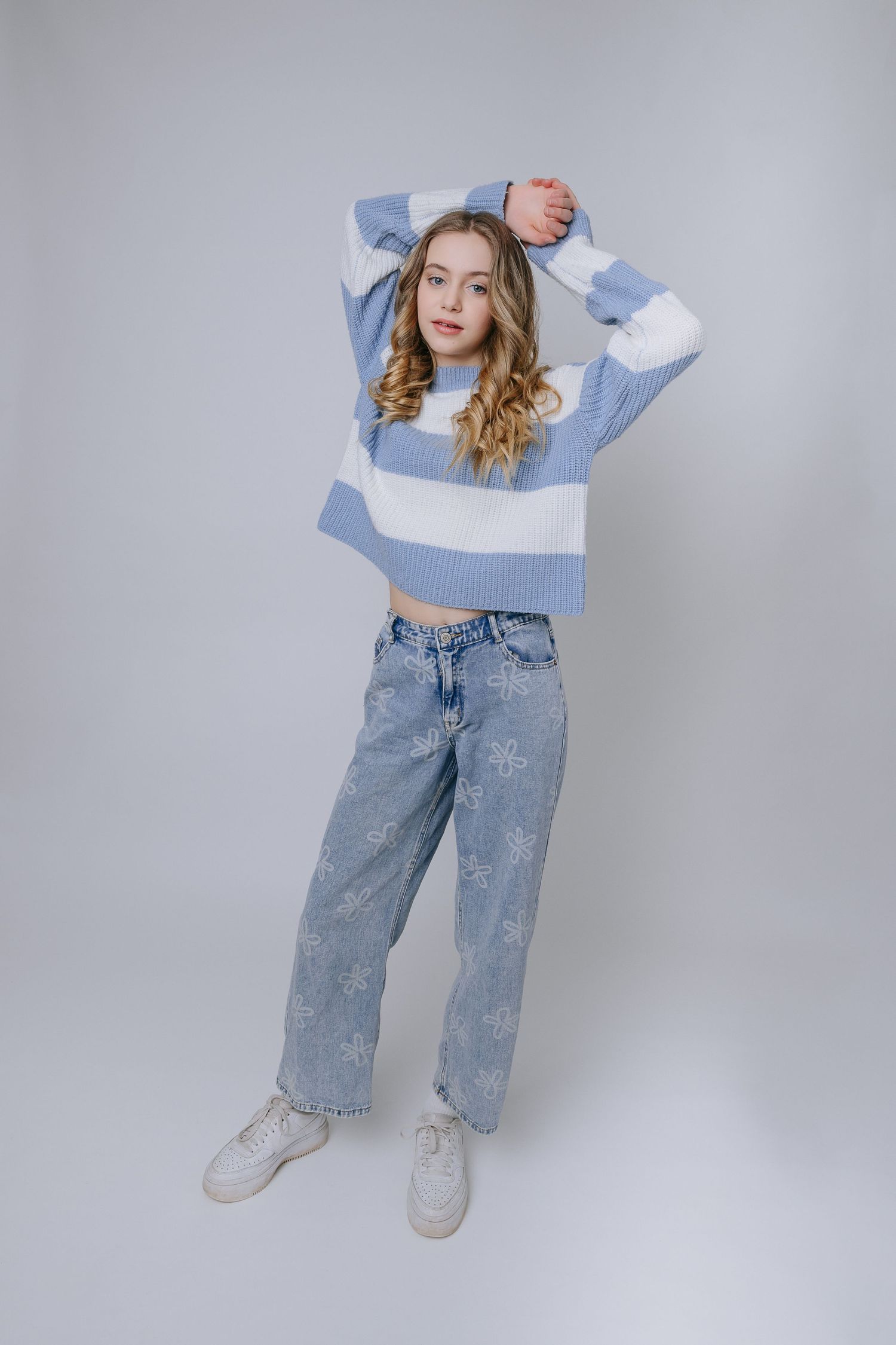 Model in light blue crop top and embellished baggy jeans poses against gray backdrop in fashion photo series.