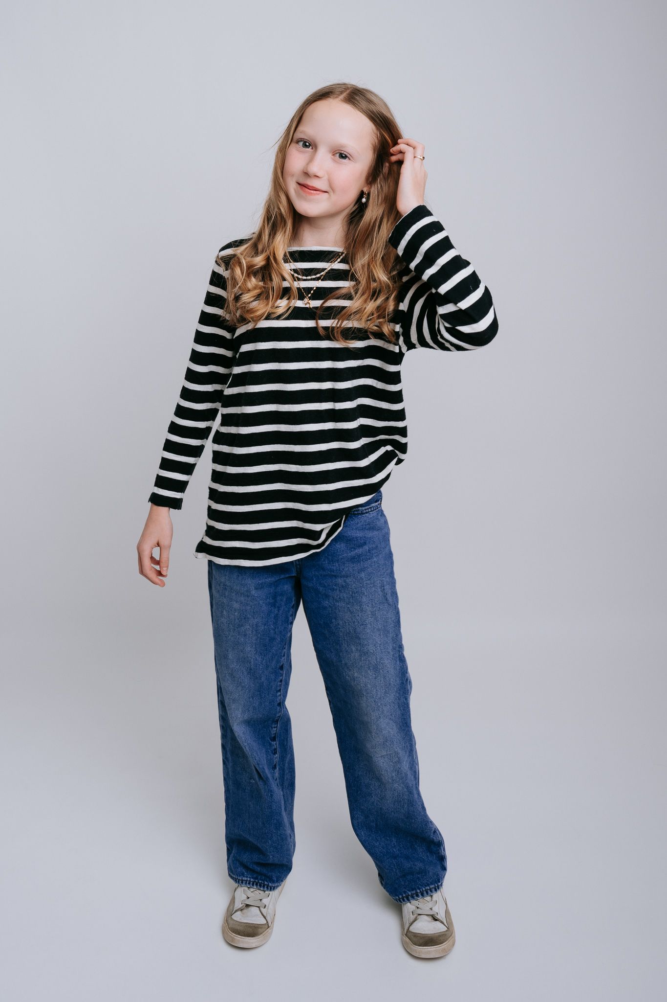 Young girl in striped black and white top and blue jeans posing confidently in a studio setting.