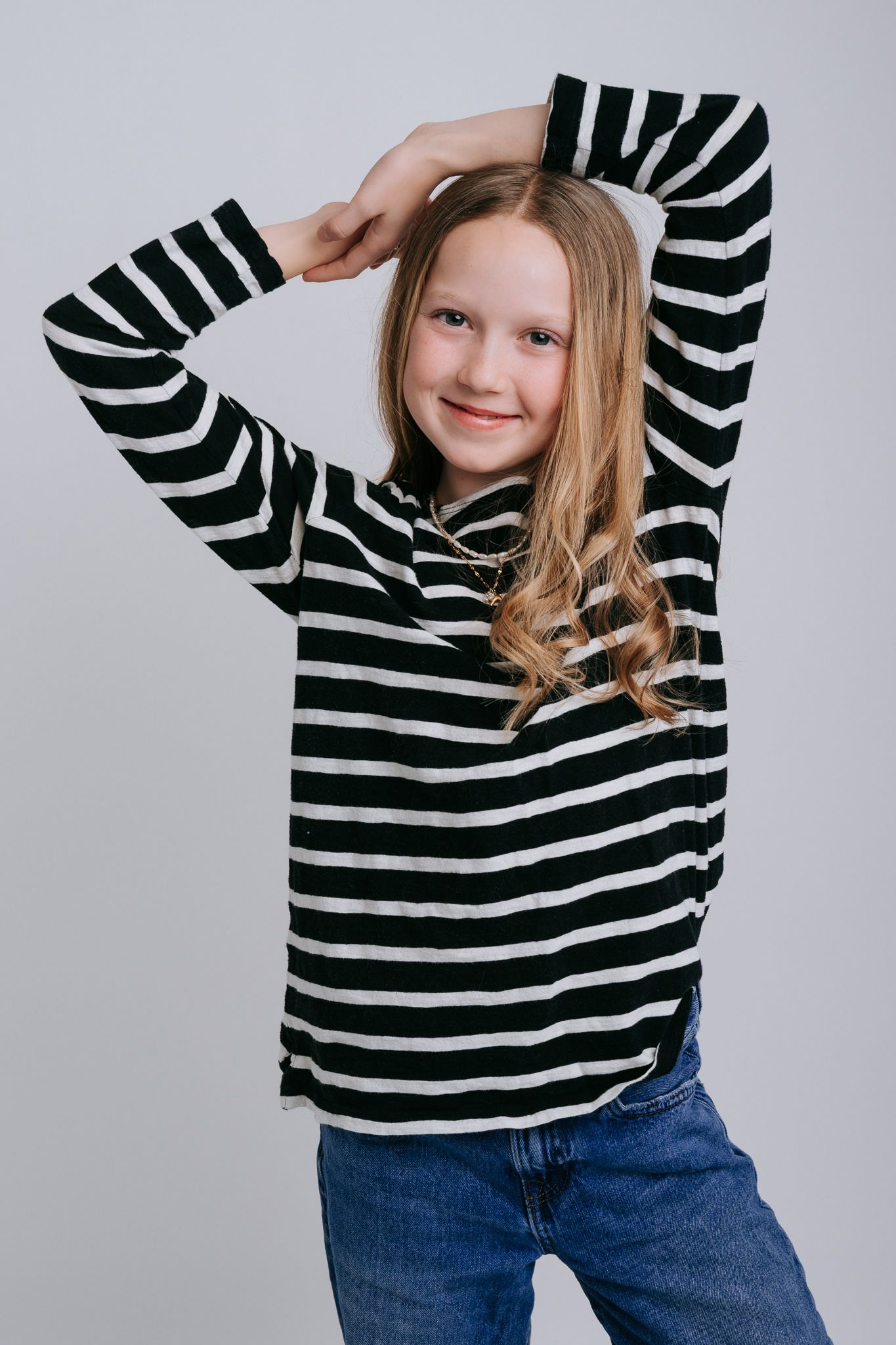 Smiling young girl with long blonde hair wearing a black and white striped long-sleeve shirt and blue jeans.