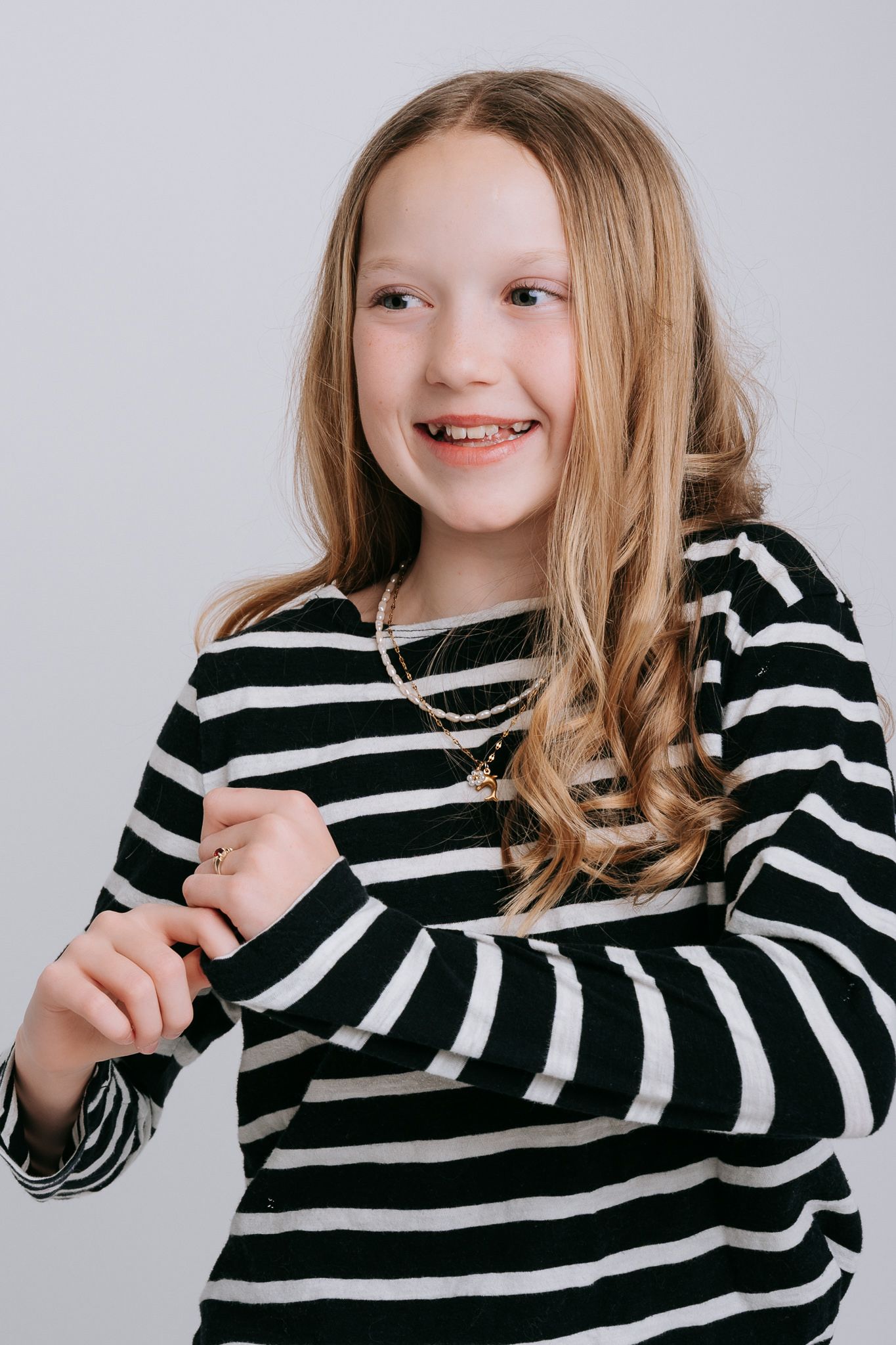 Smiling young girl with long blonde hair wearing a black and white striped long-sleeve shirt.