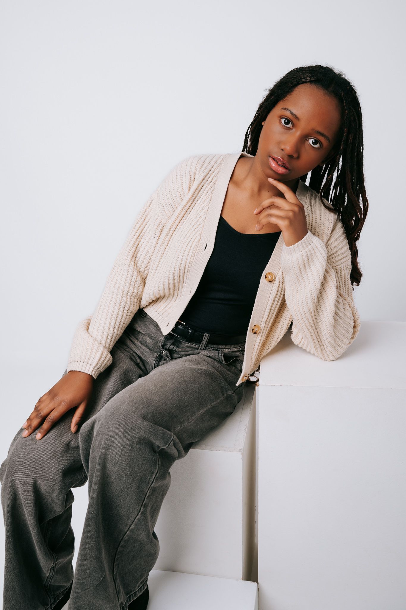 Model wearing a cozy beige cardigan with black top and gray pants poses against white background in stylish fashion series.