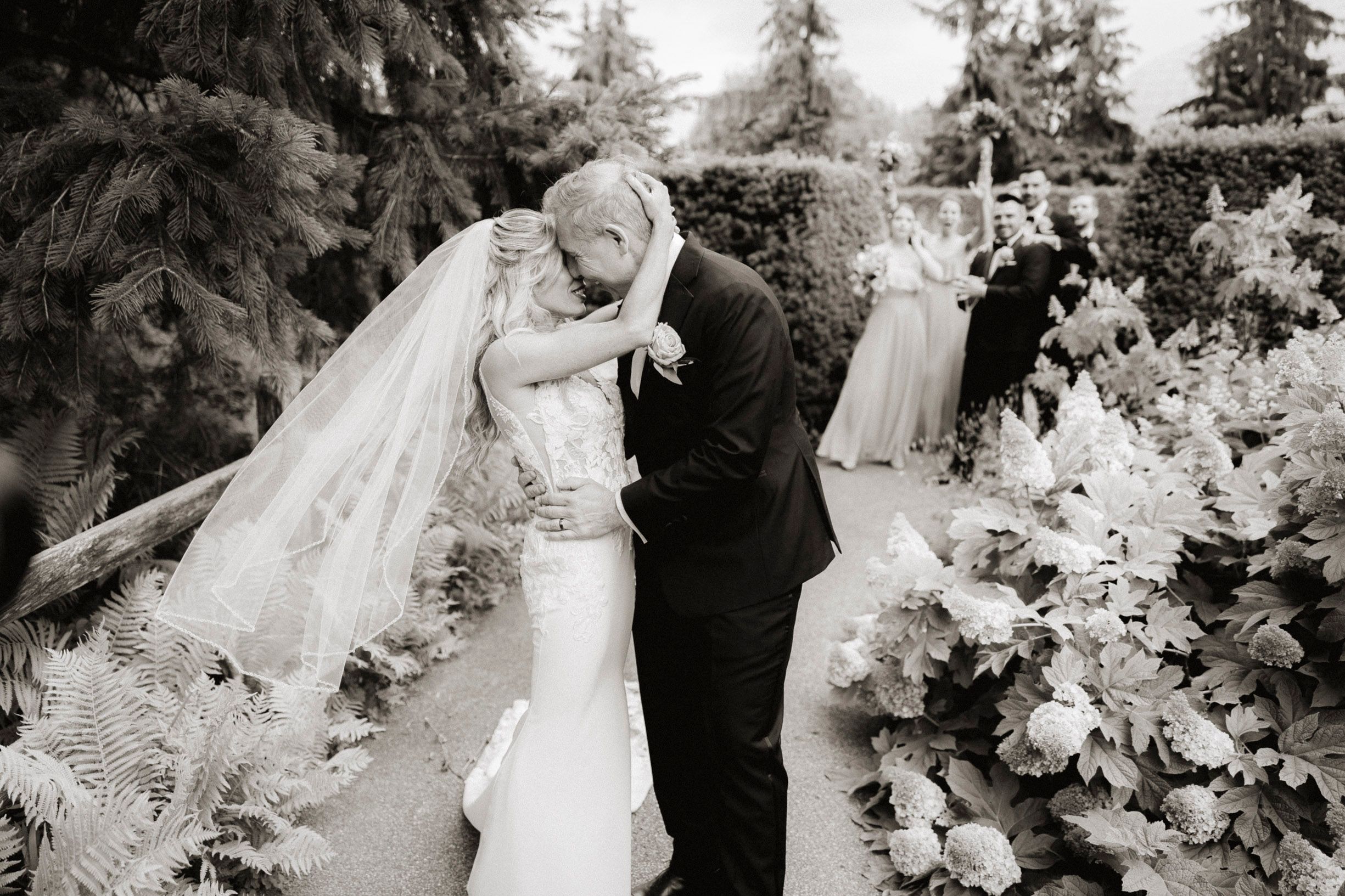 Romantic black and white wedding ceremony photo in a garden with flowing veil and floral decorations.