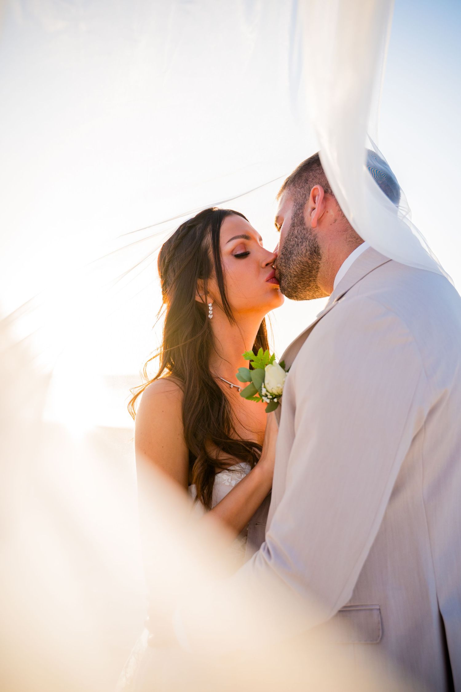 A couple in white attire walks hand in hand along a tropical beach with turquoise water and blue sky in the background.
