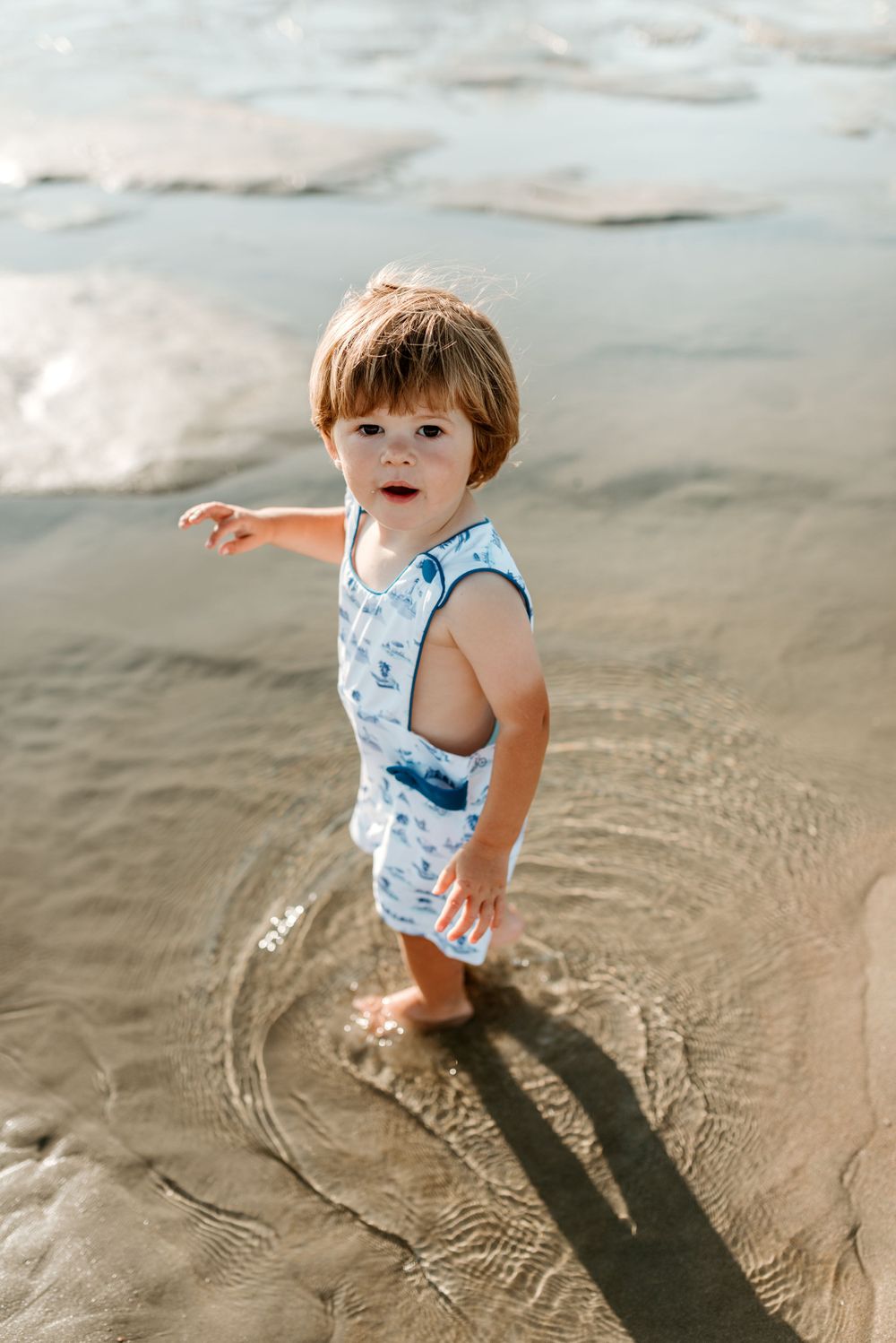 Young child playing in shallow beach water wearing blue and white patterned swimwear.