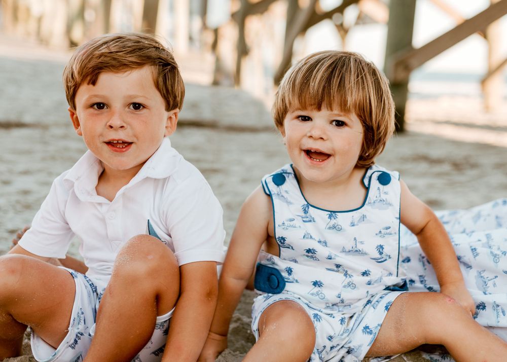 Children relaxing on beach wearing matching blue and white outfits.