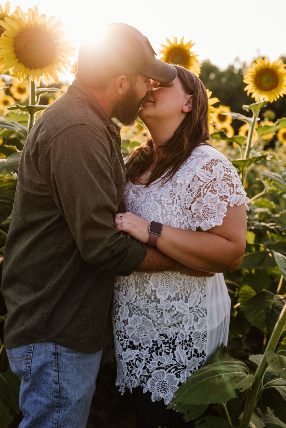 Romantic couple embraces in a sunlit sunflower field during golden hour.