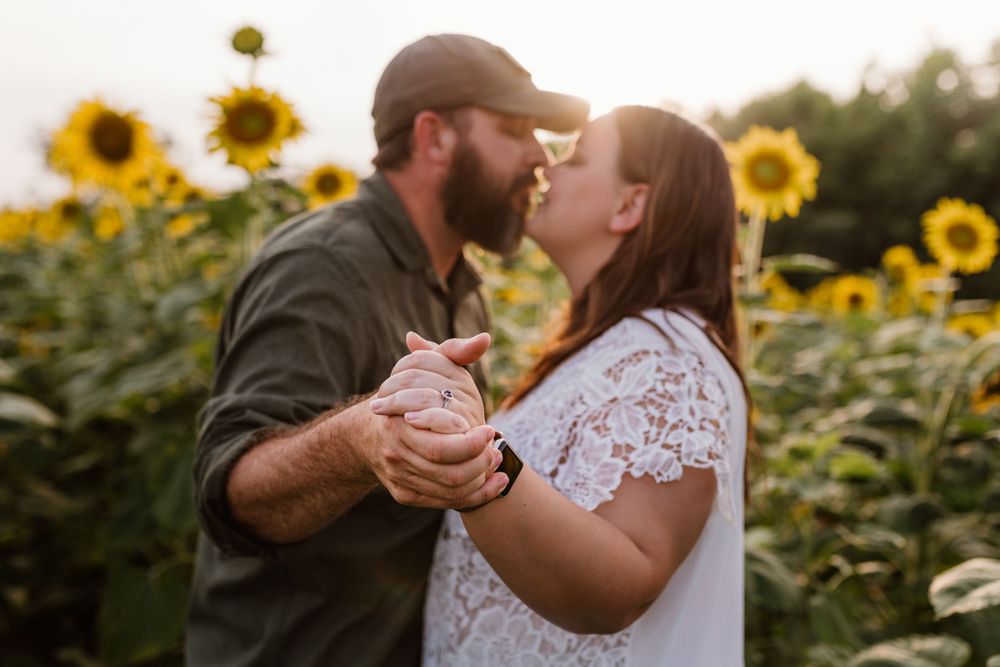 Intimate moment captured between couple surrounded by blooming sunflowers at sunset.