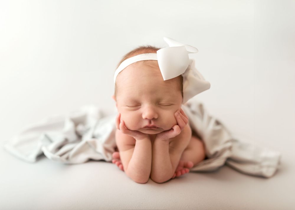 Peaceful newborn baby sleeping wrapped in soft white blanket against light background.