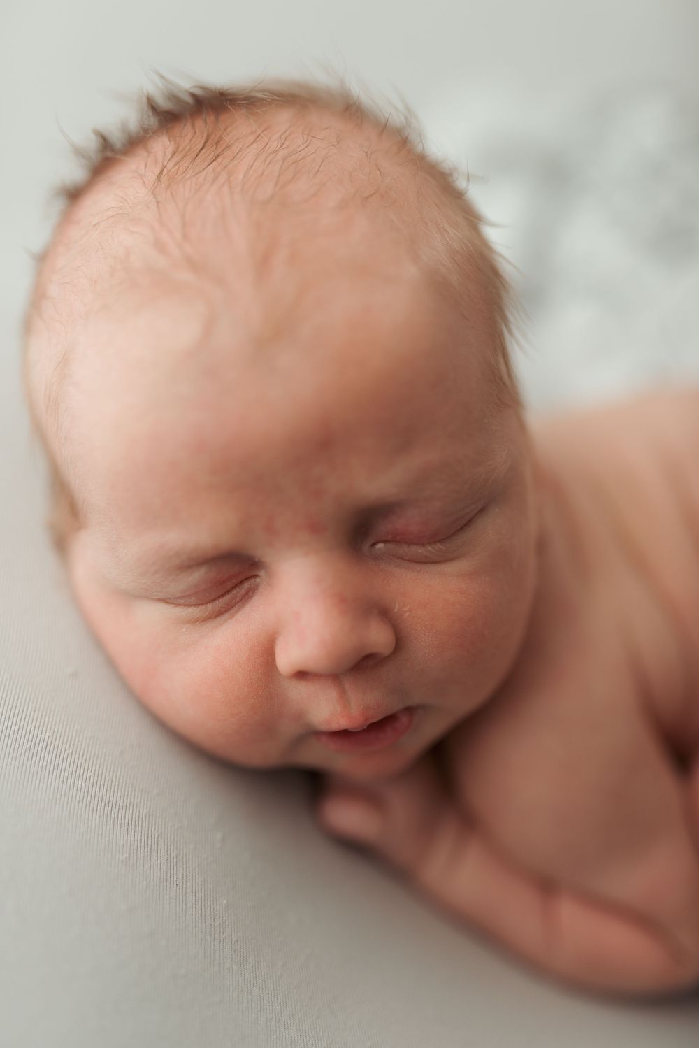 Close-up profile views of sleeping newborn baby on soft white background.