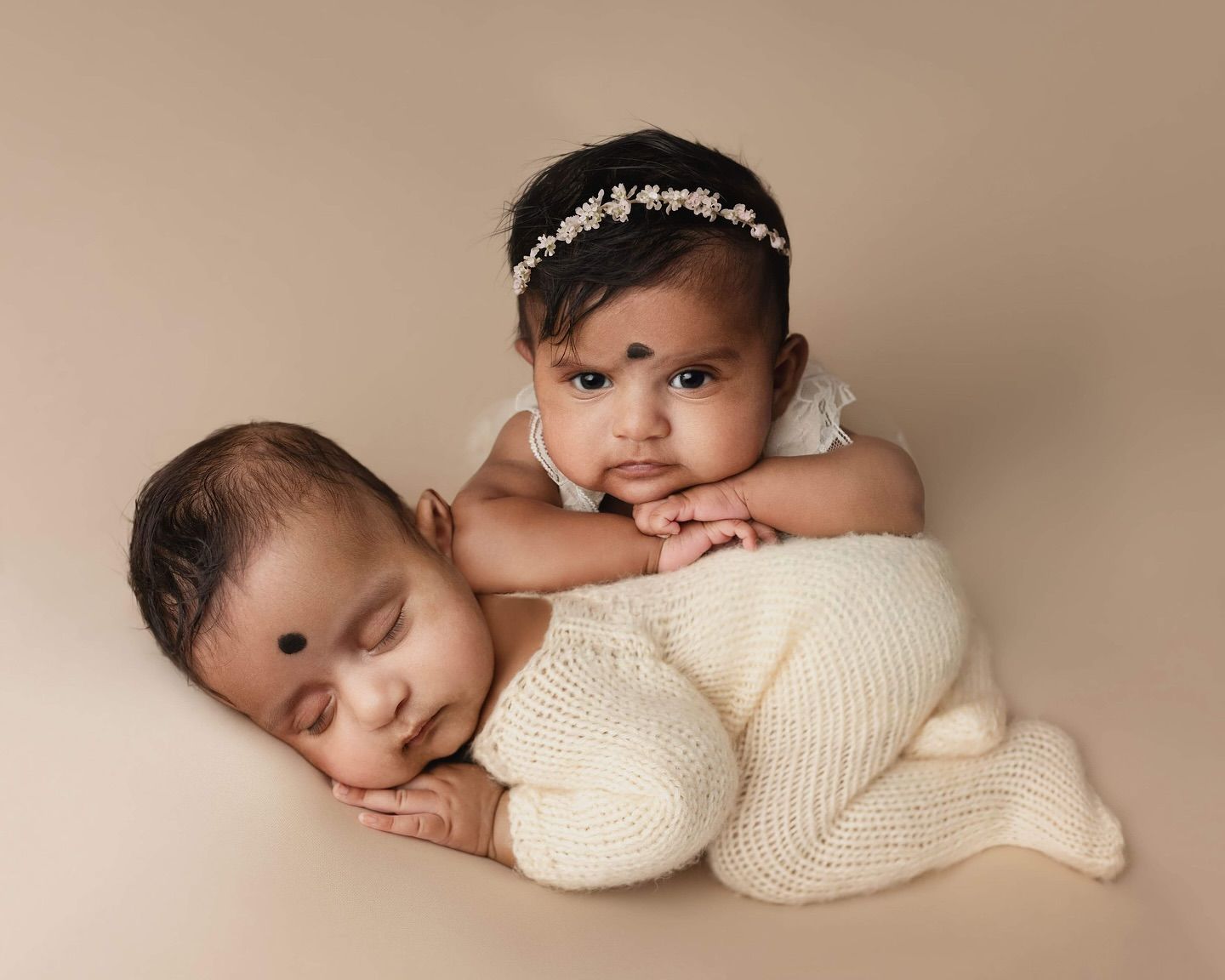 Peaceful sleeping newborn baby in cream knit sweater resting on soft beige backdrop.