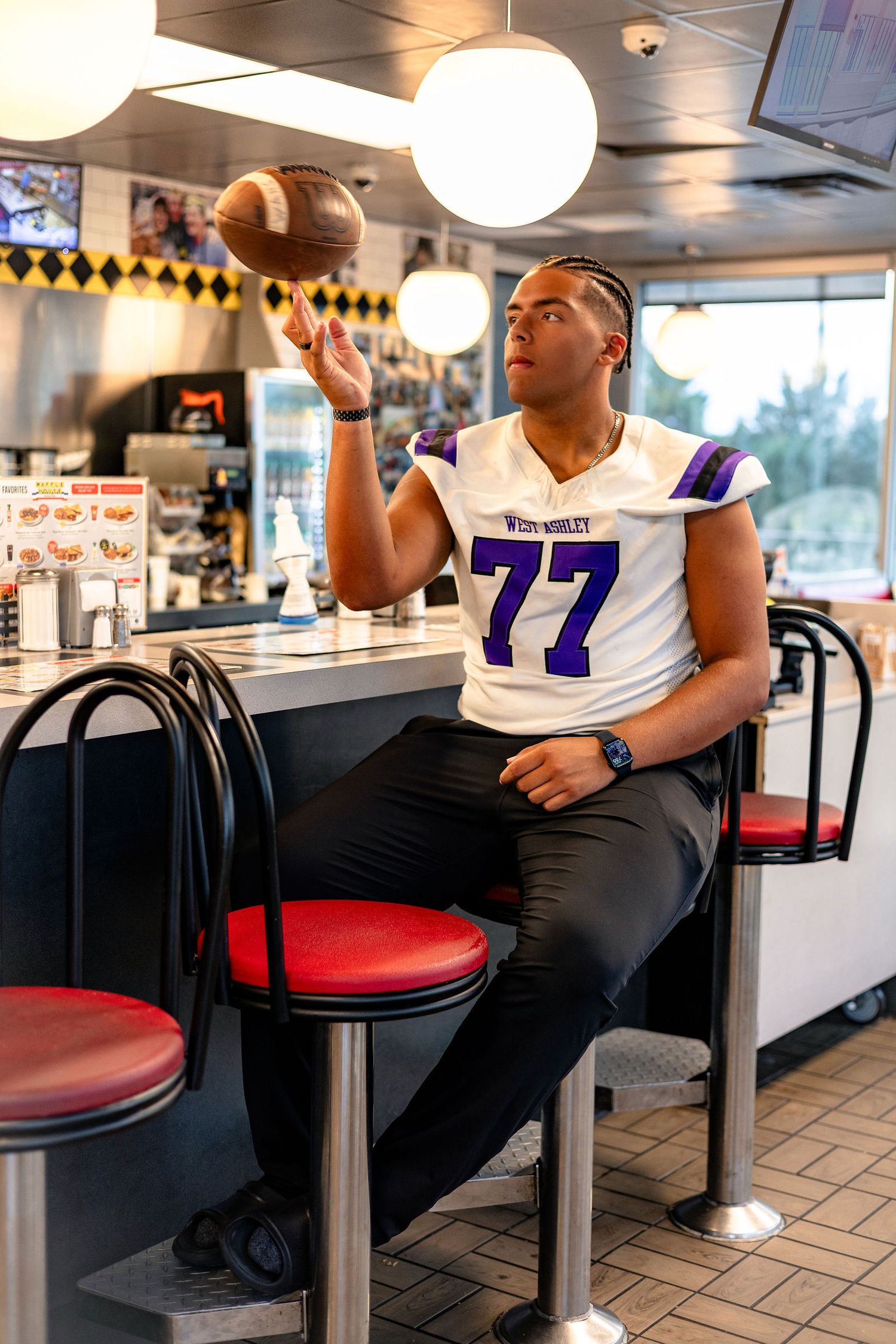 Person sitting at a diner counter with white and purple sports jersey relaxing in casual setting.