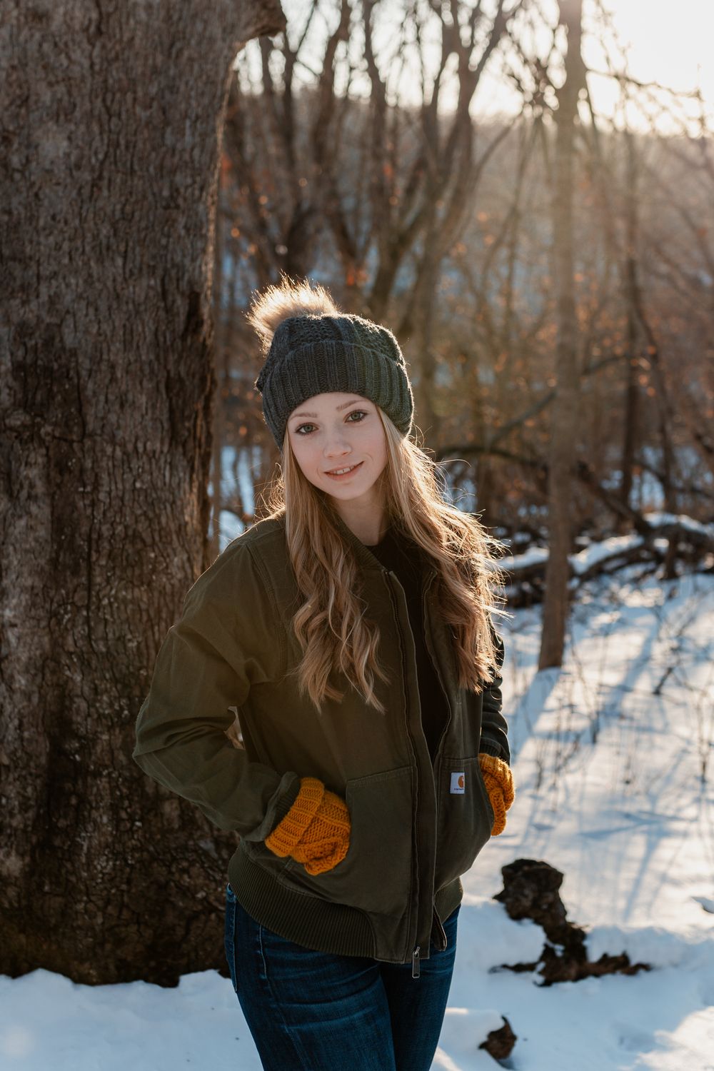 Winter portrait of someone wearing a dark knit beanie and olive jacket in a snowy forest setting.