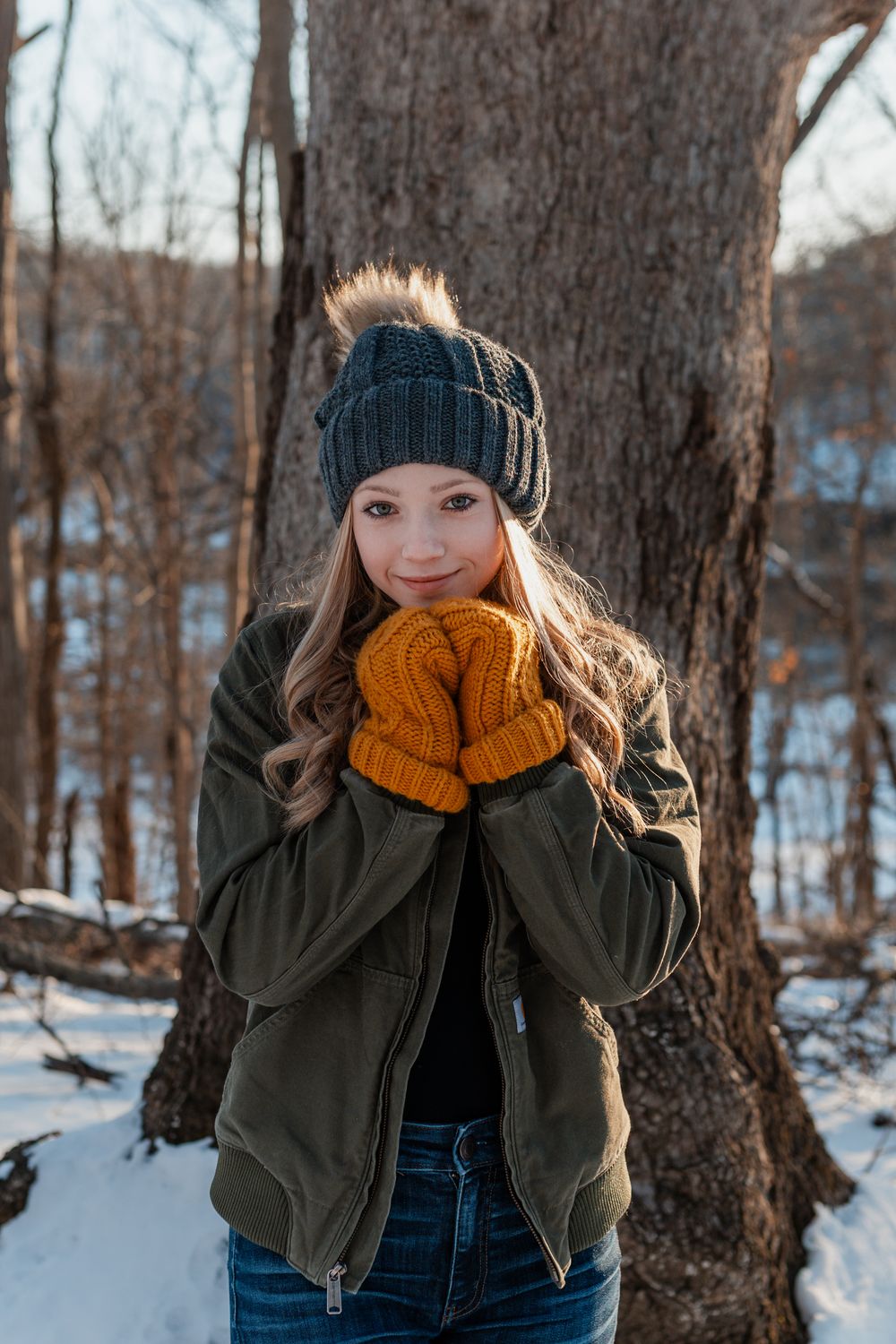 Playful winter scene with someone in an orange scarf and olive jacket against snowy trees.