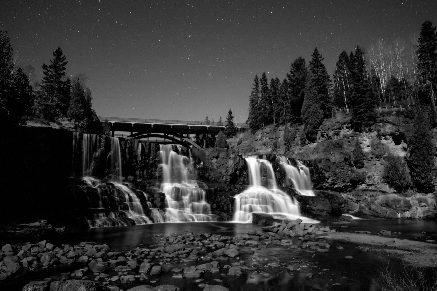 Night sky landscape black & white photography of Gooseberry Falls beneath star-filled sky on a full moon night, dramatic celestial wall art.
