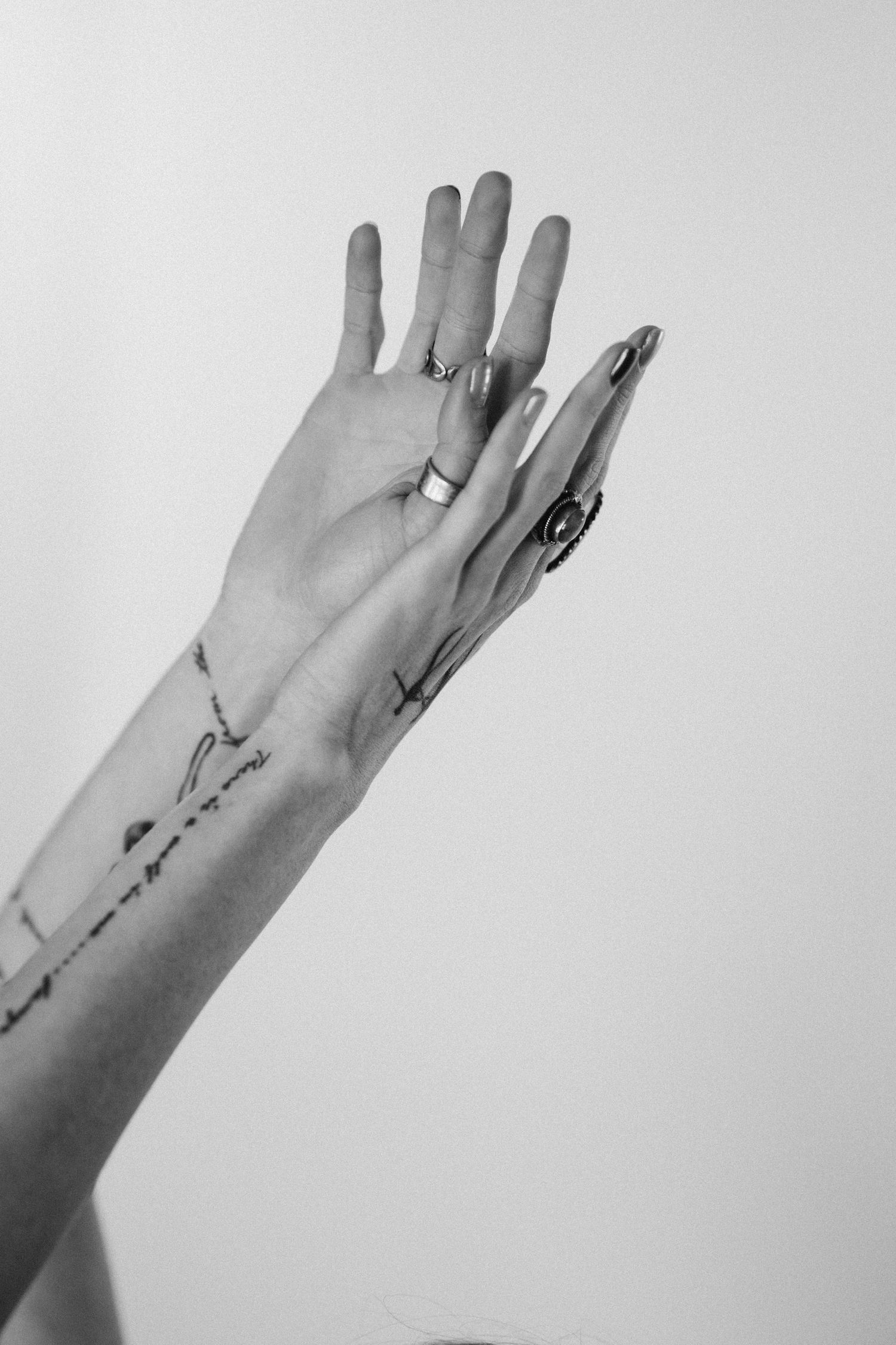 Black and white artistic photo of raised female hand adorned with rings and forearm tattoos.