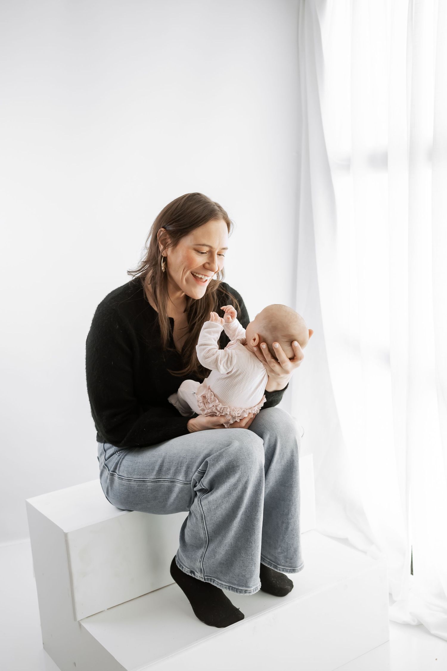 Parent and baby share joyful moments together in bright minimalist setting with white backdrop.