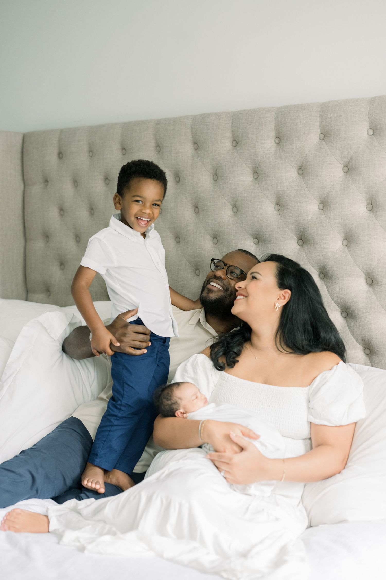 family smiling on bed with newborn at an in-home newborn session in washington dc