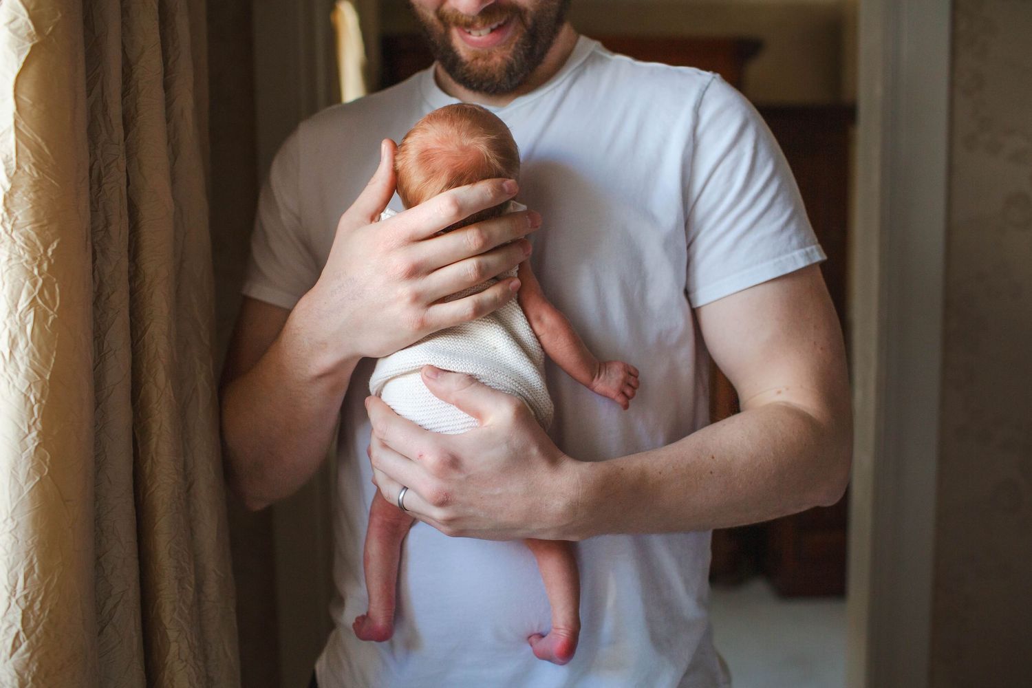 A person wearing a white t-shirt holds and comforts a small baby in a tender moment at home.