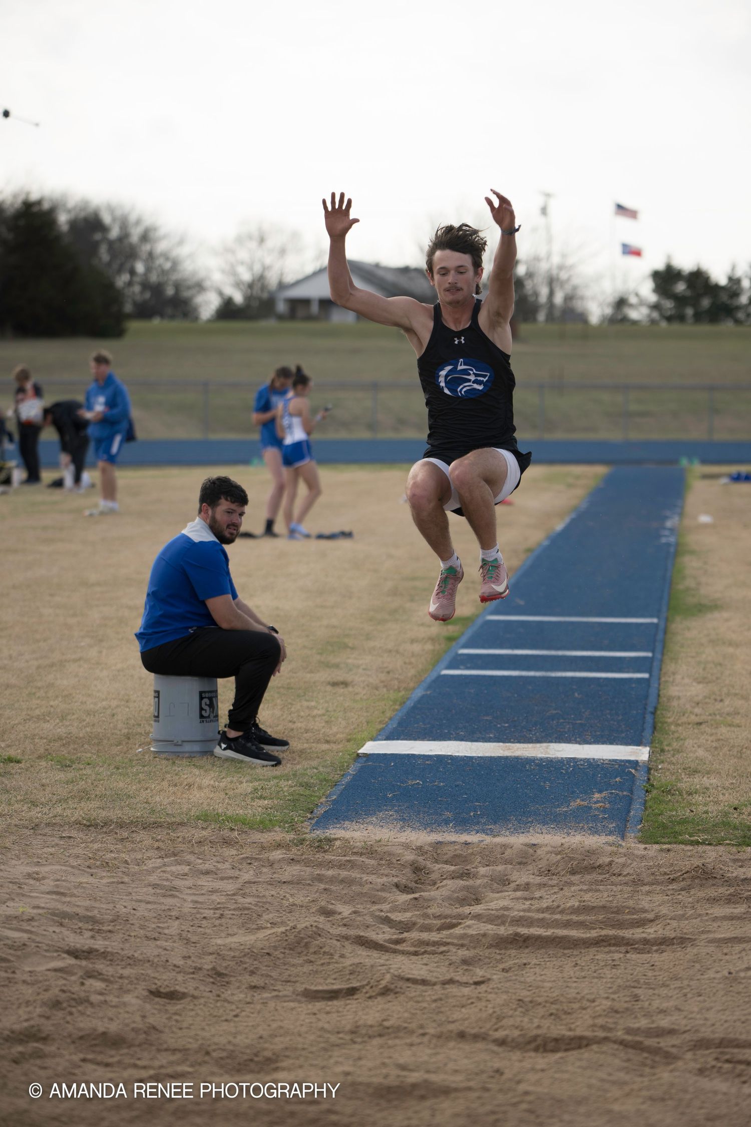 Athletes perform long jumps on a blue track during a track and field competition.