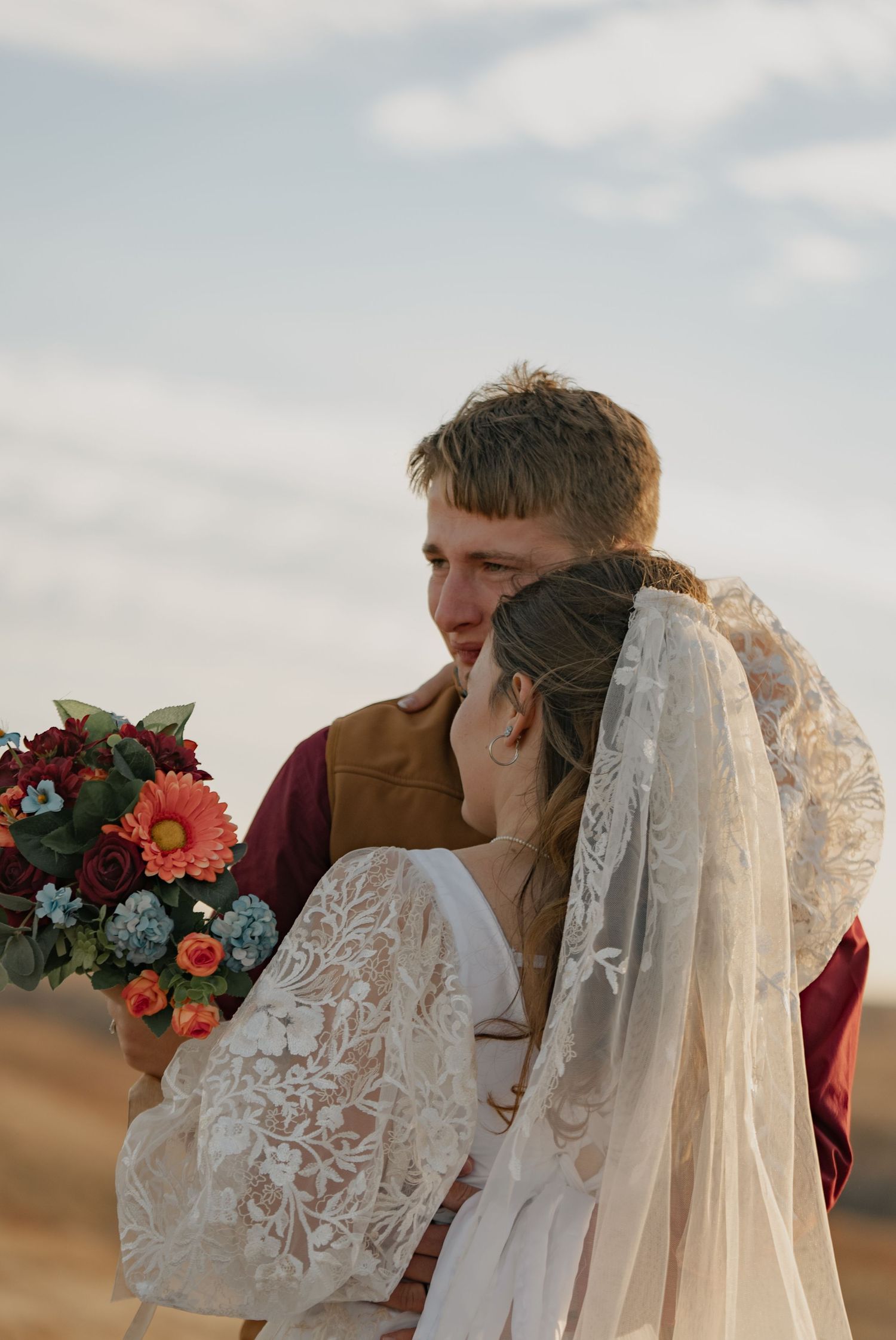 A couple poses for wedding photos in front of a vintage steam locomotive on a sunny day with blue skies.