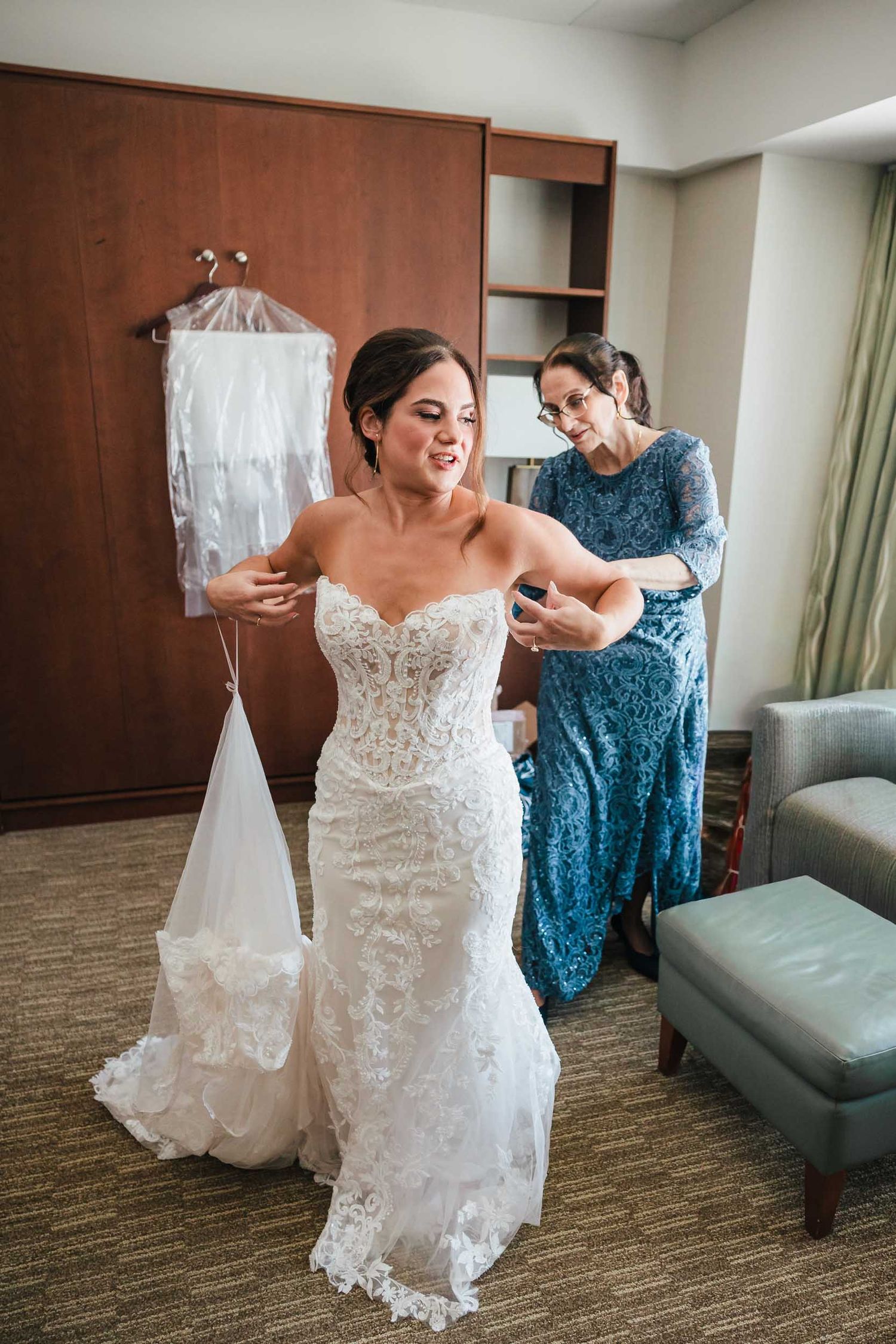 Bride putting on her lace wedding dress with help from her mother during Boston wedding preparations