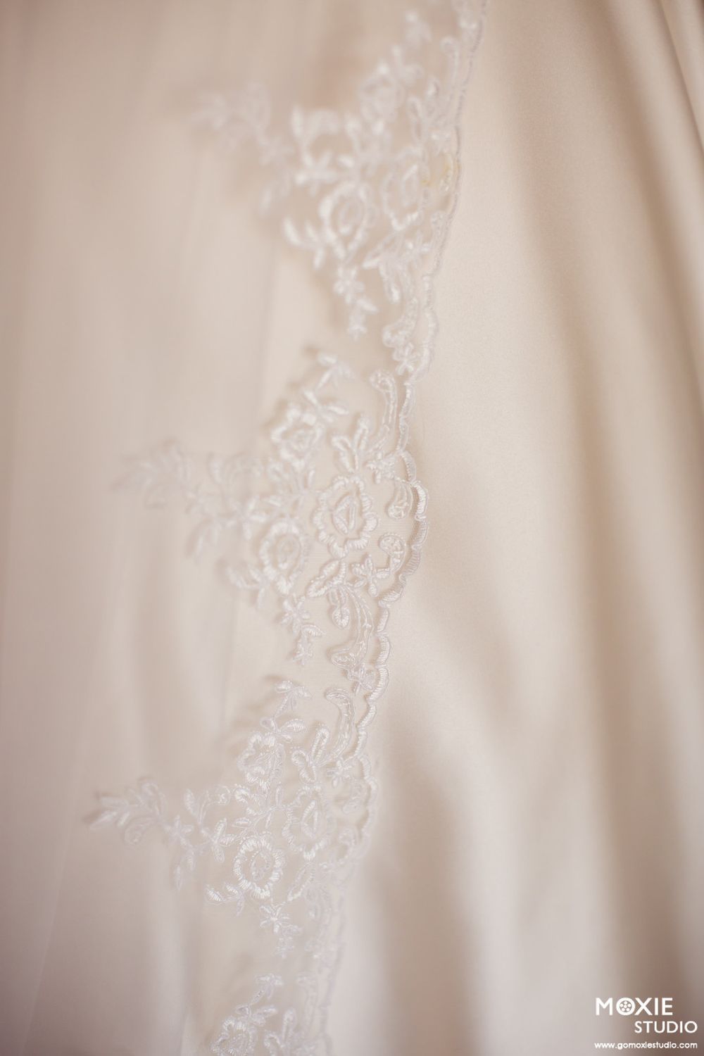 Delicate lace trim detail on ivory silk wedding dress fabric with soft focus effect.