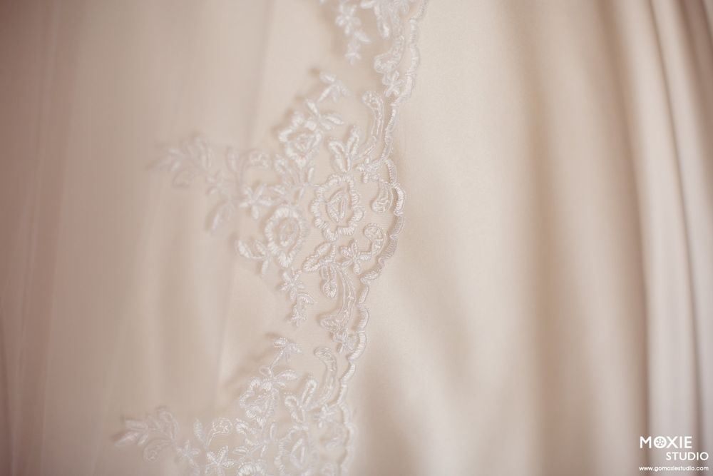 Close-up detail of delicate white lace trim on ivory satin wedding dress fabric.