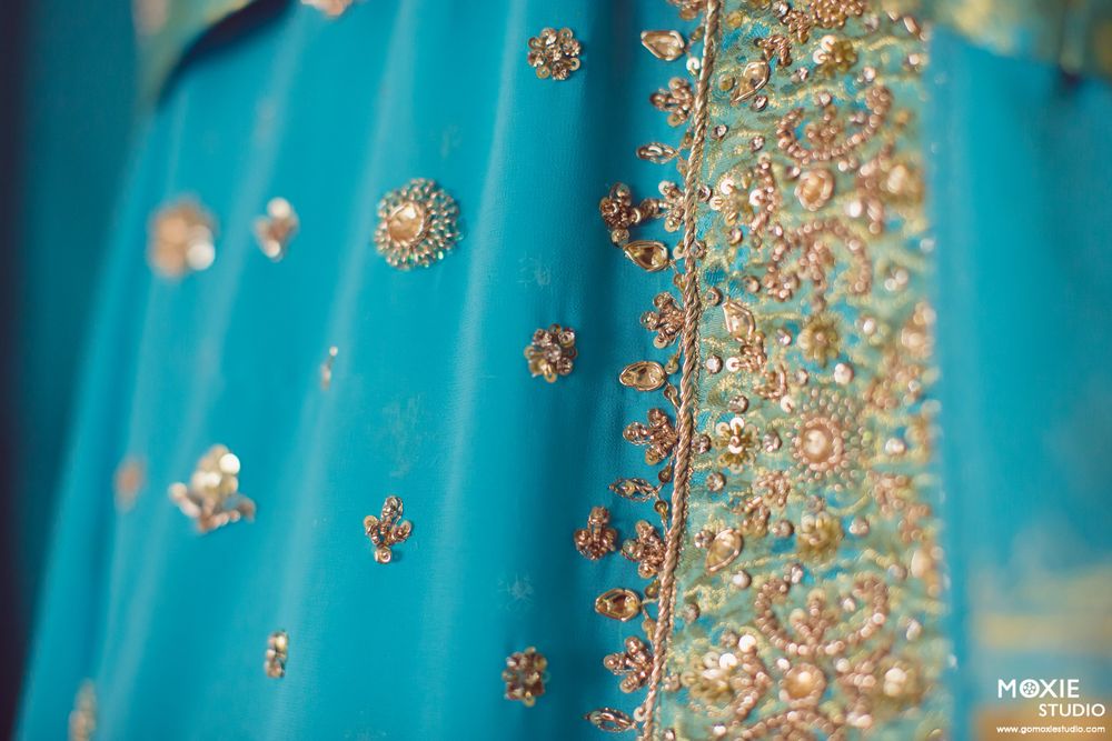 Intricate gold embroidery and beadwork details on a turquoise blue fabric with sequin accents.