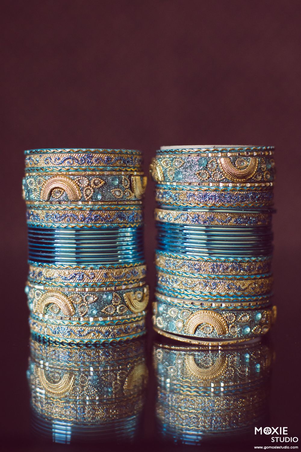 Elegant stacks of turquoise and gold Indian wedding bangles with intricate crystal detailing photographed against dark background.