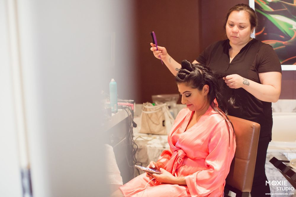 A bride getting her hair and makeup done while sitting in a preparation room before the wedding ceremony.