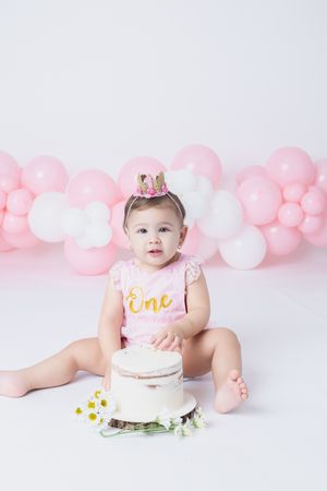 First birthday setup with cake, pink and white balloons, and festive decorations.