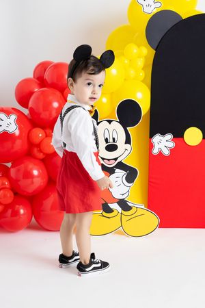 Mickey Mouse themed photoshoot with child against balloon backdrop.