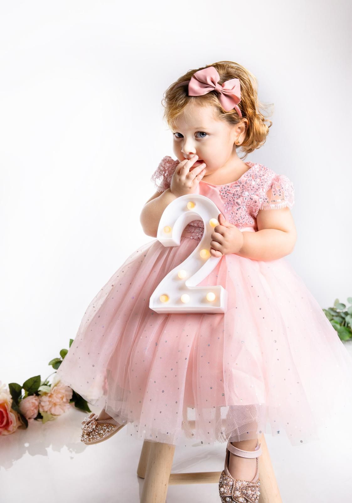Toddler in pink tulle dress holding illuminated number two.