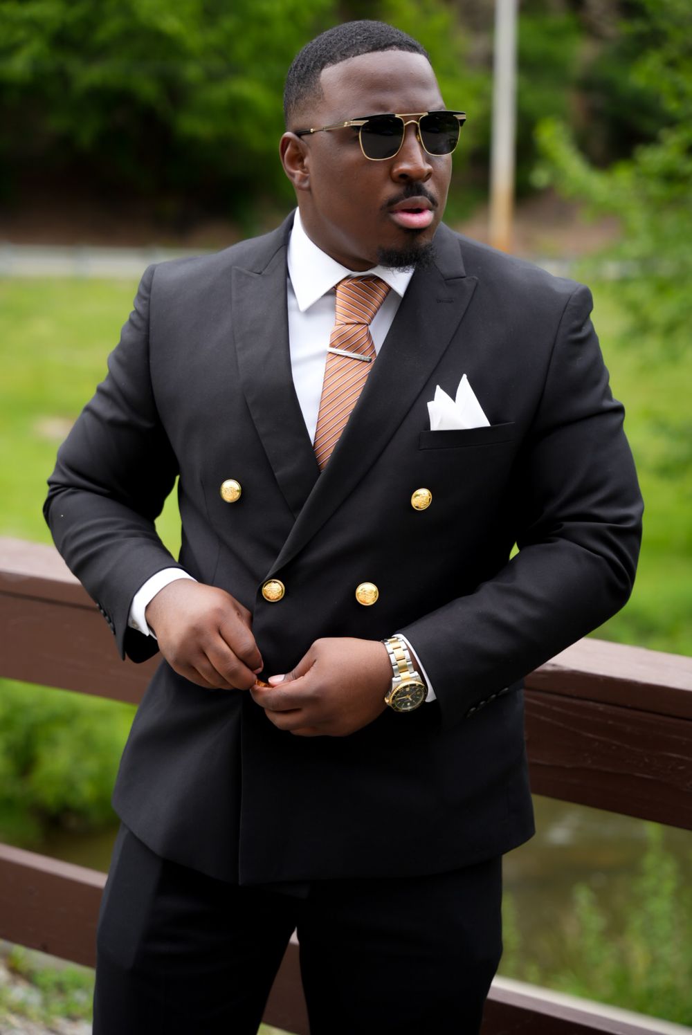 Professional fashion portrait showing details of a black double-breasted suit with gold buttons and peach tie.