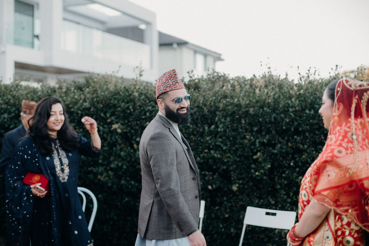 Outdoor wedding ceremony scene with cultural attire against a modern architectural backdrop.