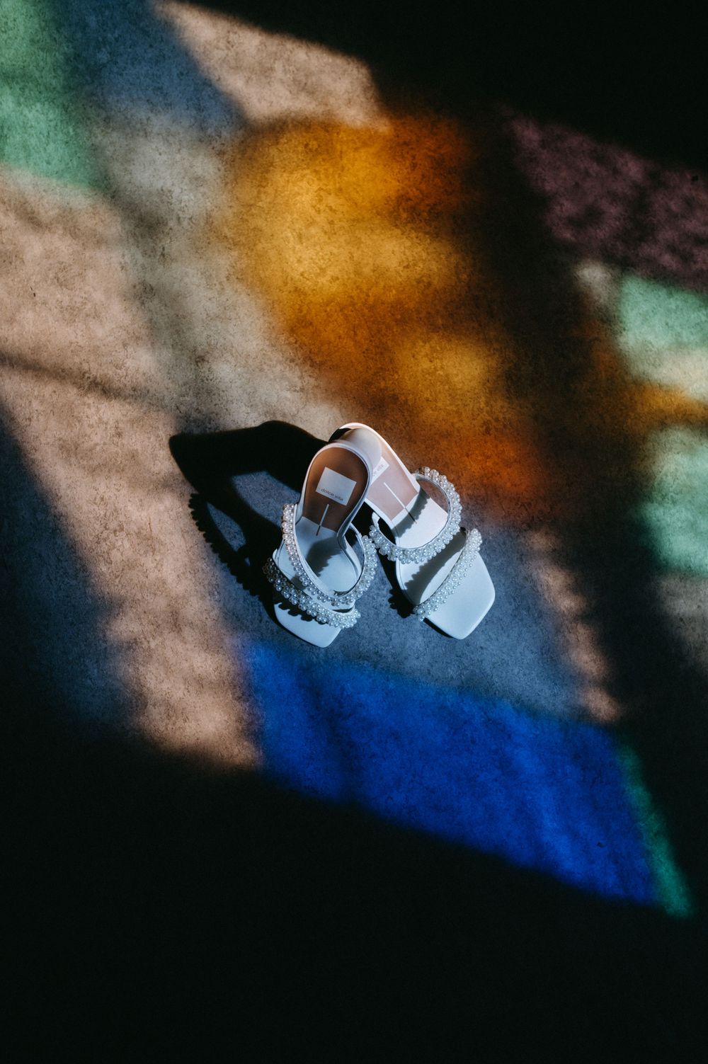 White bridal sandals on colorful stained glass reflection background.