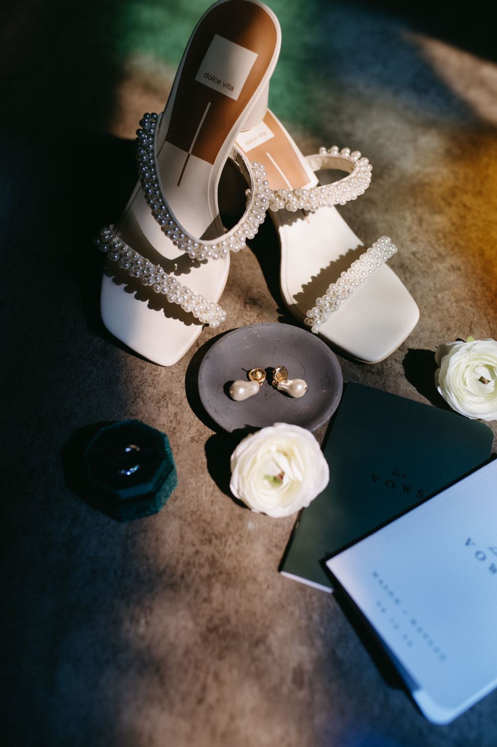 Wedding shoes and rings arranged with white roses in artistic lighting.