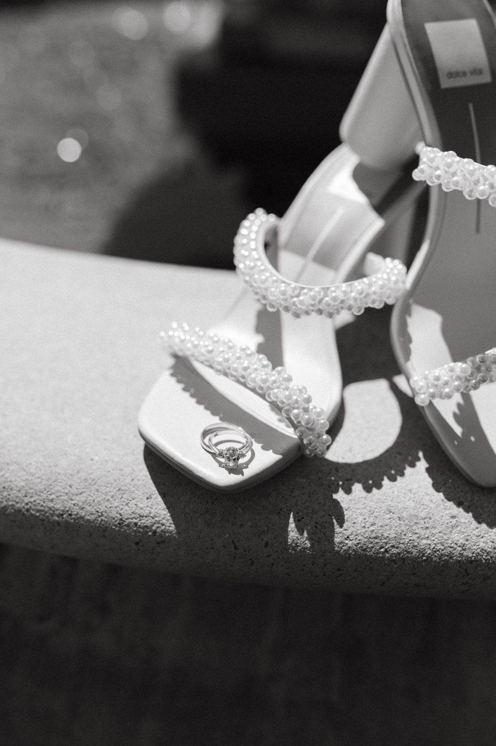 Elegant white bridal shoes with pearl beaded straps displayed in black and white photography.
