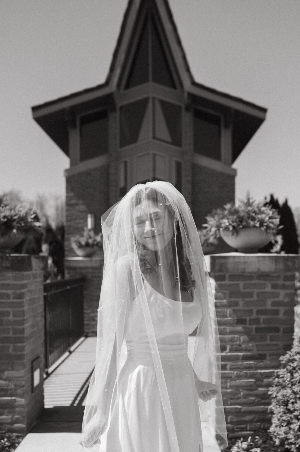 Black and white photo of veiled bride standing in front of octagonal tower building.