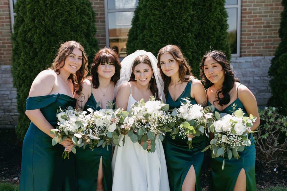 Bridal party holding white floral bouquets while posing in front of cypress trees.