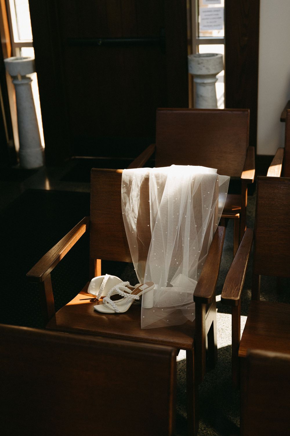 White wedding veil draped over a wooden chair in dramatic lighting.