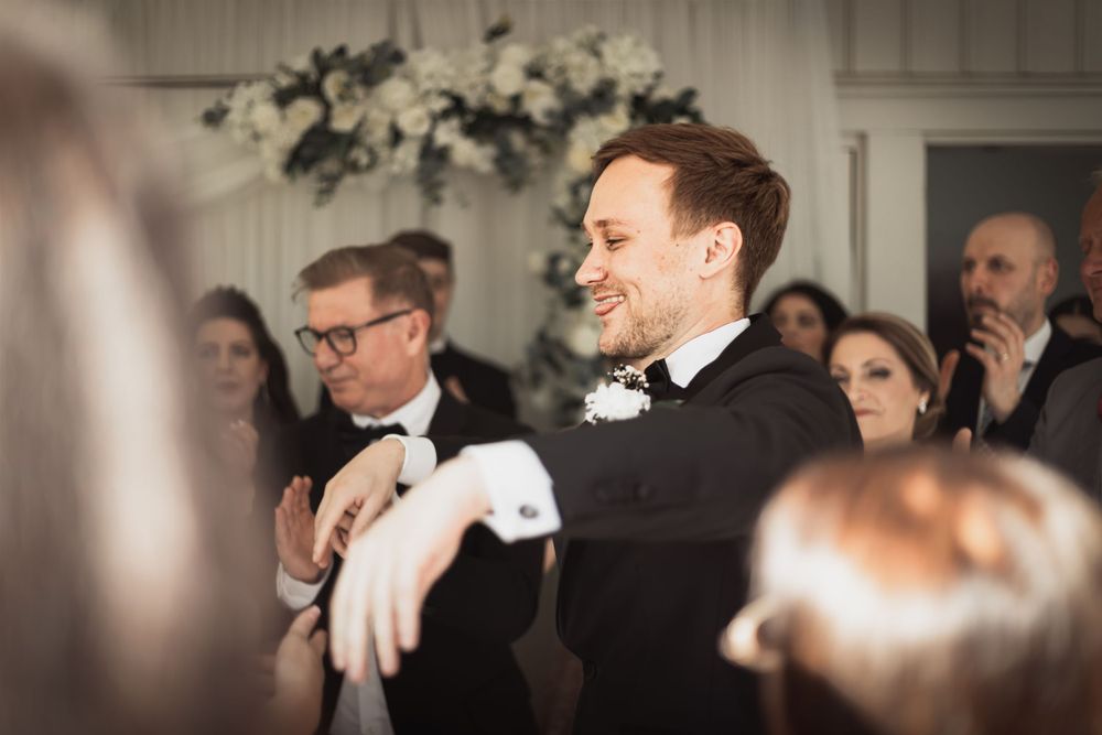 Brudgum i smoking dansar med gäster i festlig bröllopsmiljö med blommor