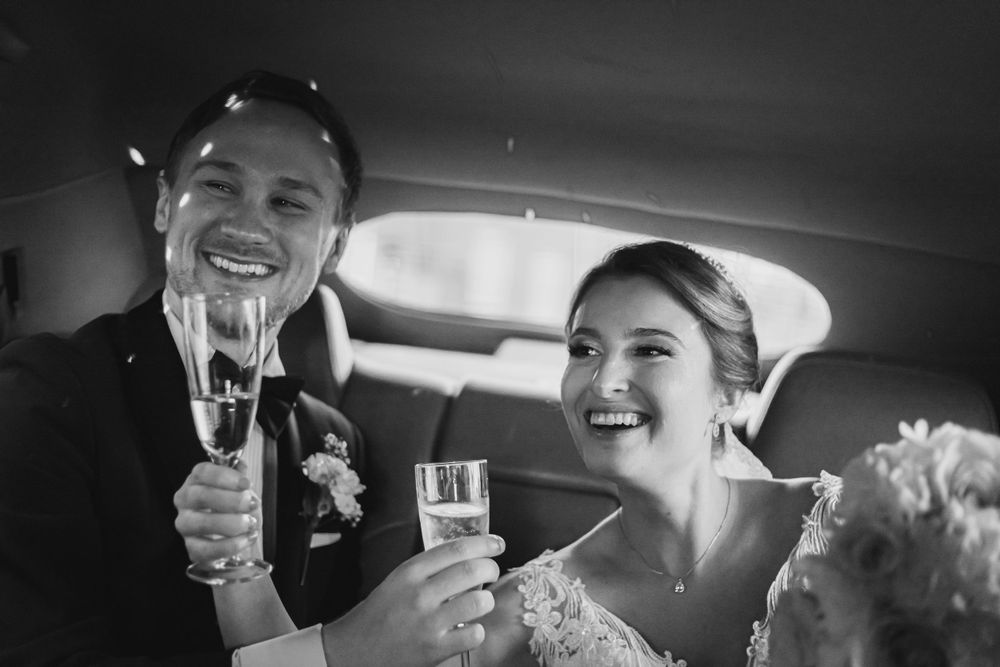 Brudpar i smoking och klänning skålar med champagne i svartvit bröllopsbild