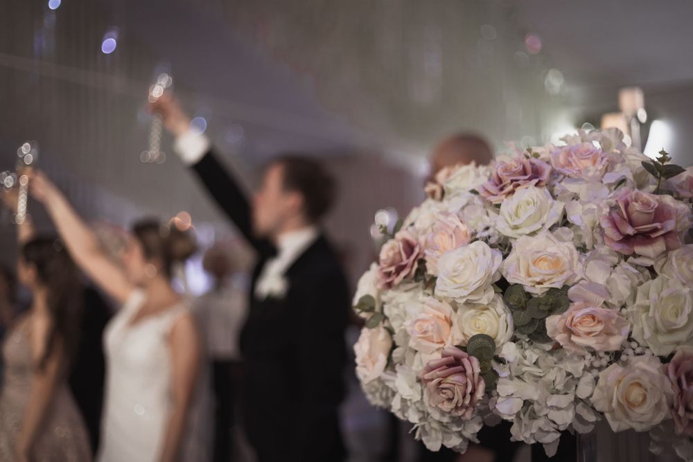 Bröllopsfest med gäster som skålar och blomsterarrangemang i förgrunden