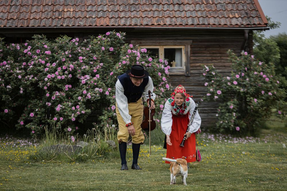 Par i traditionella folkdräkter med fiol i lantlig miljö med stuga
