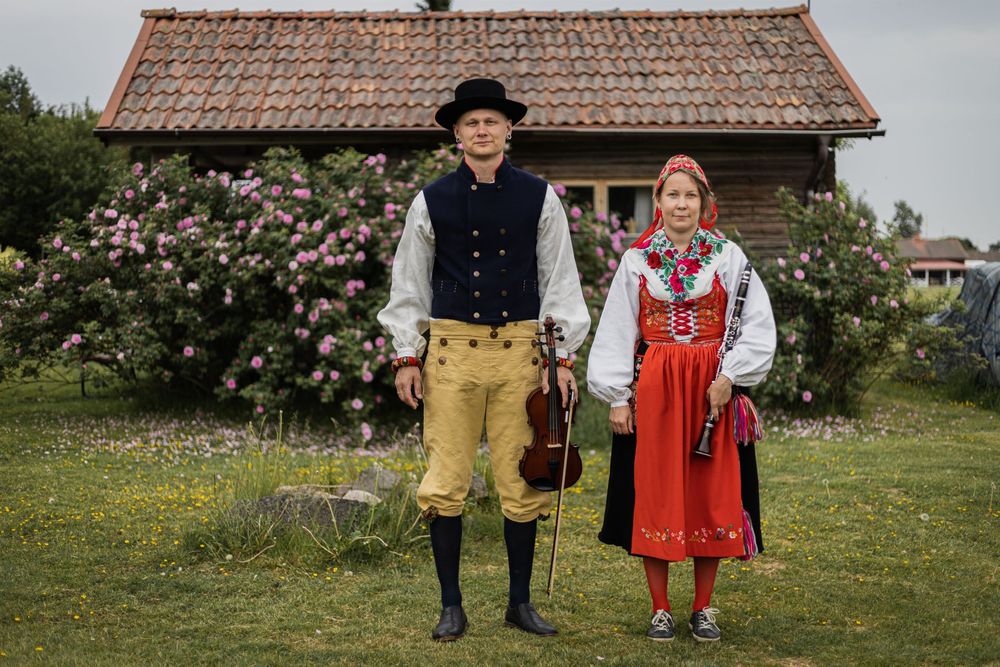 Par i traditionella folkdräkter med fiol i lantlig miljö med stuga