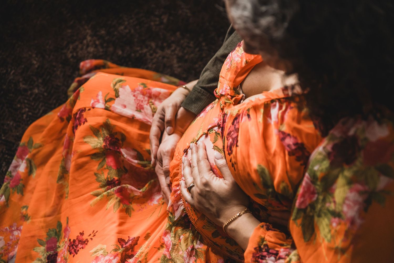 Close-up detail of a flowing orange floral maternity dress in dramatic lighting.