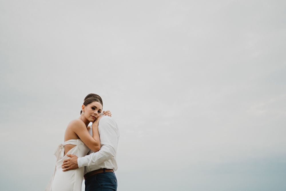 Bride with a serious expression, hugging her partner against a sky backdrop